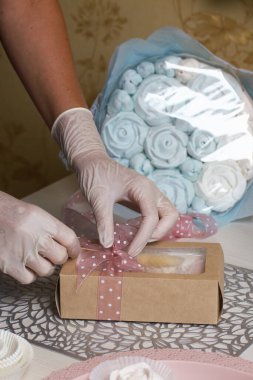 Bir kadın ev yapımı marşmelov paketini kurdele ve lagurularla süslüyor. Yakınlarda marşmelov gülleri ve laleler var. Yakın çekim..