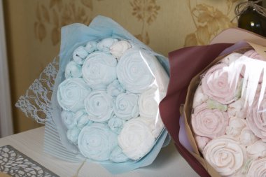 Marshmallow buketleri el işi paketlemede. Marşmelov gülleri ve lalelerden oluşuyor. Buketler masa yüzeyinde yatıyor..