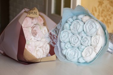 Marshmallow buketleri el işi paketlemede. Marşmelov gülleri ve lalelerden oluşuyor. Buketler masa yüzeyinde yatıyor..