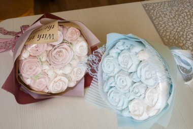 Marshmallow buketleri el işi paketlemede. Marşmelov gülleri ve lalelerden oluşuyor. Buketler masa yüzeyinde yatıyor..