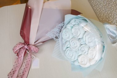 Marshmallow buketleri el işi paketlemede. Marşmelov gülleri ve lalelerden oluşuyor. Buketler masa yüzeyinde yatıyor..