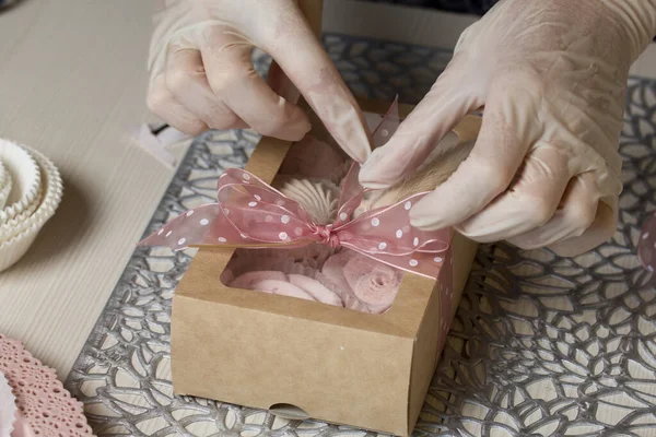 Bir kadın el işi ambalajında şekerleme paketliyor. Fiyonka kurdele bağlar. Yakın çekim..