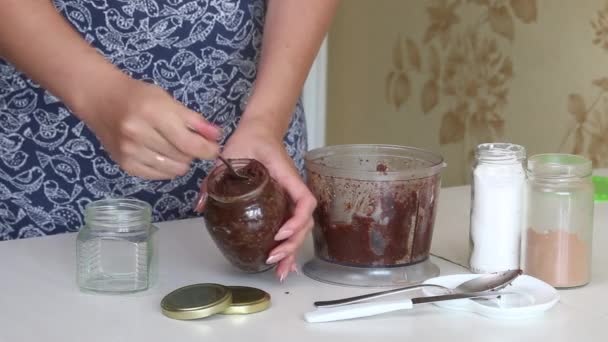 A woman puts nut butter from a blender bowl into a jar. Closes it with a lid. Walnut urbech. The ingredients are on the table side by side — Stock Video