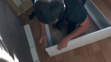 Adam mobilyaların parçalarını birbirine doğruluyor. Evde mobilya topluyor. Diğer parçalar yere saçılmış. Yukarıdan çekilen..