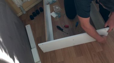 Adam mobilyaların parçalarını birbirine doğruluyor. Evde mobilya topluyor. Diğer parçalar yere saçılmış. Yukarıdan çekilen.