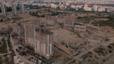 Modern bir şehir bloğunun inşaat alanı. Yüksek binalar yapım aşamasında. İnşaat kulesi vinçleri. Gün batımında hava fotoğrafçılığı.