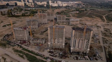 Modern bir şehir bloğunun inşaat alanı. Yüksek binalar yapım aşamasında. İnşaat kulesi vinçleri. Gün batımında hava fotoğrafçılığı.