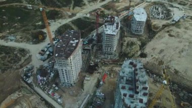 Modern bir şehir bloğunun inşaat alanı. Yüksek binalar yapım aşamasında. İnşaat kulesi vinçleri. Gün batımında hava fotoğrafçılığı.