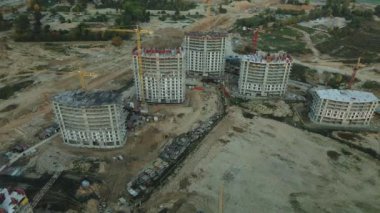 Modern bir şehir bloğunun inşaat alanı. Yüksek binalar yapım aşamasında. İnşaat kulesi vinçleri. Gün batımında hava fotoğrafçılığı.
