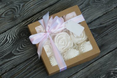 Hediye kutusunda ev yapımı marşmelov. Fiyonka bağlanmış bir kurdeleyle bağlanmış. Siyah çam tahtalarında.