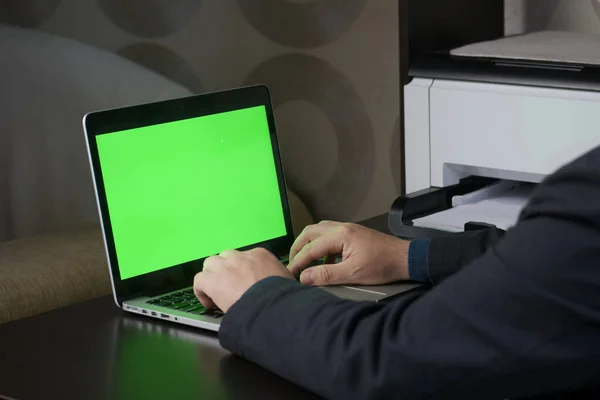 A man works at a laptop with a green screen. Chromakey.