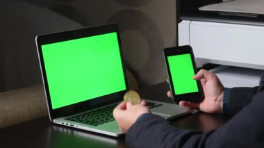 Yeşil ekranlı bir adam dizüstü bilgisayarda çalışıyor. Elinde yeşil ekran olan bir akıllı telefon tutuyor. Şifreli para olarak kabul ediyor. Kromakey.