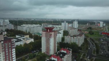 Bulutlu havada şehir üzerinde uçuş. Çok katlı binalar ve banliyölerde sarı yapraklı ağaçlar. Bulutlarla kaplanmış gri gökyüzü. Hava fotoğrafçılığı.