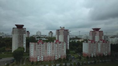 Bulutlu havada şehir üzerinde uçuş. Çok katlı binalar ve banliyölerde sarı yapraklı ağaçlar. Bulutlarla kaplanmış gri gökyüzü. Hava fotoğrafçılığı.