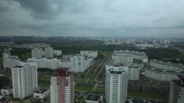 Bulutlu havada şehir üzerinde uçuş. Çok katlı binalar ve banliyölerde sarı yapraklı ağaçlar. Bulutlarla kaplanmış gri gökyüzü. Hava fotoğrafçılığı.