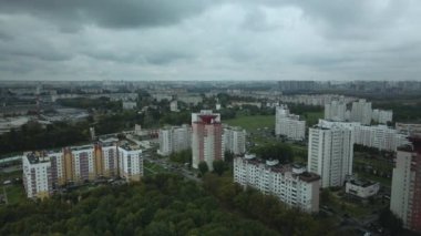 Bulutlu havada şehir üzerinde uçuş. Çok katlı binalar ve banliyölerde sarı yapraklı ağaçlar. Bulutlarla kaplanmış gri gökyüzü. Hava fotoğrafçılığı.