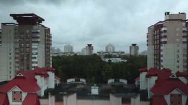 Bulutlu havada şehir üzerinde uçuş. Çok katlı binalar ve banliyölerde sarı yapraklı ağaçlar. Bulutlarla kaplanmış gri gökyüzü. Hava fotoğrafçılığı.