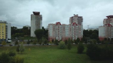 Bulutlu havada şehir üzerinde uçuş. Çok katlı binalar ve banliyölerde sarı yapraklı ağaçlar. Bulutlarla kaplanmış gri gökyüzü. Hava fotoğrafçılığı.