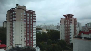 Bulutlu havada şehir üzerinde uçuş. Çok katlı binalar ve banliyölerde sarı yapraklı ağaçlar. Bulutlarla kaplanmış gri gökyüzü. Hava fotoğrafçılığı.
