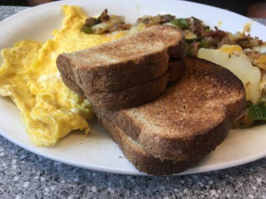 Amerika 'nın küçük bir kasabasında bir lokantada kahvaltı. Yumurtalı omlet, tam buğday tostu ve beyaz tabakta ev usulü patates, bir restoran. Bir lokantada kahvaltı..