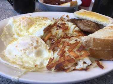 Az pişmiş iki yumurta, kızarmış et, tost ve sosisli börek yerel lokantada benekli bir formika masasında kahvaltıda. Brunch için 1950 'lerin tarzı restoran. Tipik Amerikan kahvaltısı..
