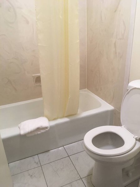 Hotel bathroom in a clean, newly renovated local motel.  White tub, toilet,  and tile.  Tub shower with off white shower curtain.