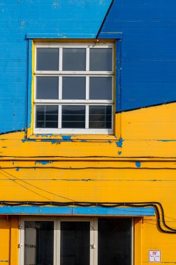 Sarı-mavi-cyan ön cephede beyaz çerçeveli pencereler..