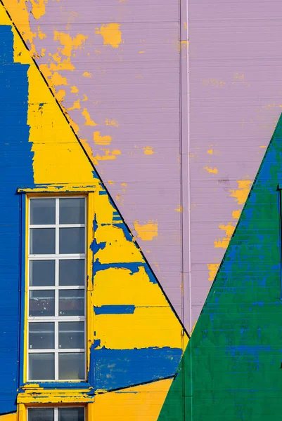 A white-framed window on a shabby facade painted in yellow, purple, green and blue with abstract designs.