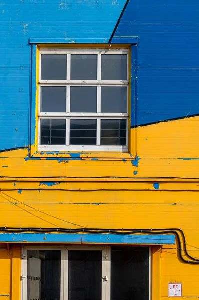 Sarı-mavi-cyan ön cephede beyaz çerçeveli pencereler..