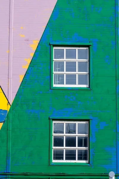 Soyulmuş yeşil, mavi, mor ve sarı renklerle soyulmuş bir cephede beyaz çerçeveli pencereler..