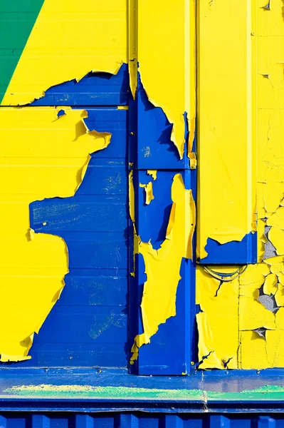 Mavi lekeli ön cephenin bir parçası soyulmuş sarı-yeşil boyanın altından dışarı bakıyor ve soyut bir desen oluşturuyor..