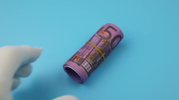 La main dans un gant blanc ramasse des billets de 500 euros roulés sur un fond bleu — Video