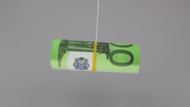 Загорнуті 100 євро банкноти обертаються на нитці на сірому фоні, крупним планом — стокове відео