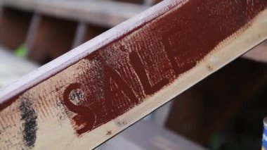 Bir işçi, satılık yazıyı kahverengi ahşap korkuluklara çiziyor.