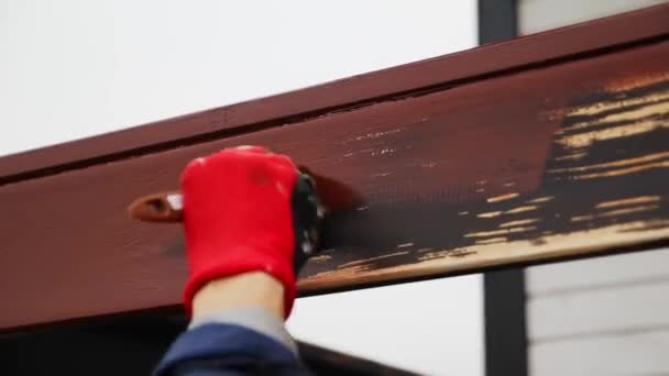 Жінка в червоних робочих рукавичках фарбує пензлем дерев'яний поручень коричневий в домашніх умовах — стокове відео