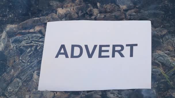 Word Adverteren op een wit vel papier brandt in een vuur tegen. Langzame beweging — Stockvideo