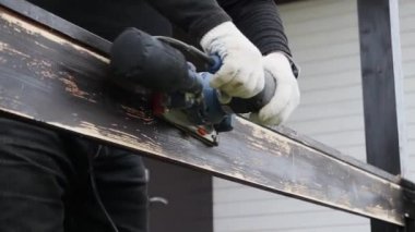 Bir işçi, evin yanında bir zımpara makinesiyle ahşap korkulukları inceliyor.