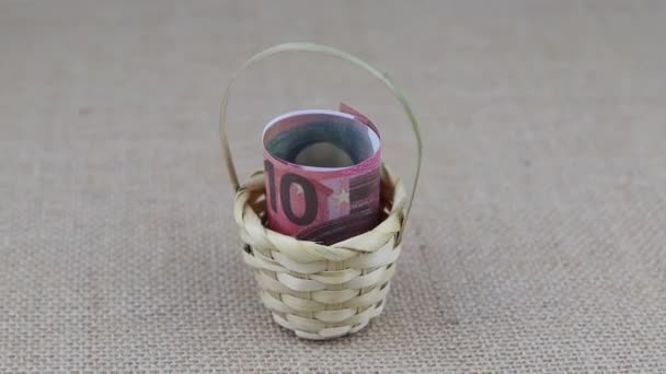 Rolled 10 euro banknotes placed in a small basket rotate on a round table — Stock Video