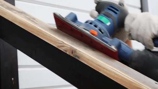 Εργαζόμενος αλέθει την κεκλιμένη επιφάνεια ενός ξύλινου κιγκλιδώματος με μια δονούμενη μηχανή — Αρχείο Βίντεο