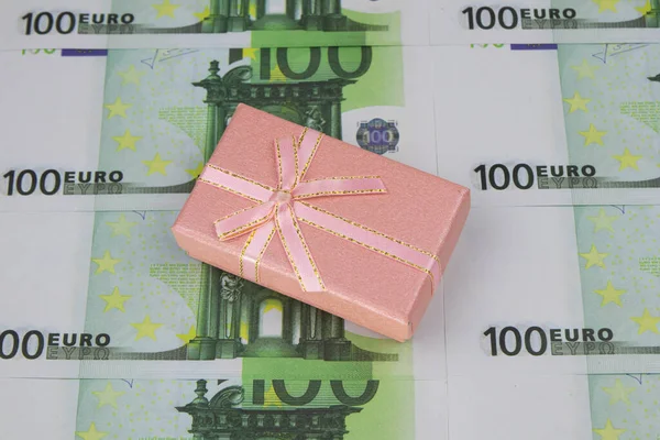 A caixa de presente cor-de-rosa encontra-se em notas de 100 euros alinhadas sucessivamente. Close-up — Fotografia de Stock