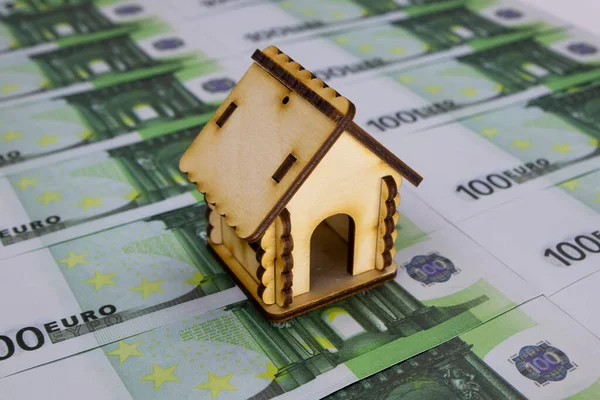 Sıraya dizilmiş 100 Euro 'luk banknotların üzerinde küçük bir ahşap ev duruyor.