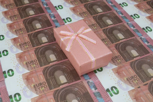 Le coffret cadeau rose repose sur 10 billets de banque en euros alignés. — Photo