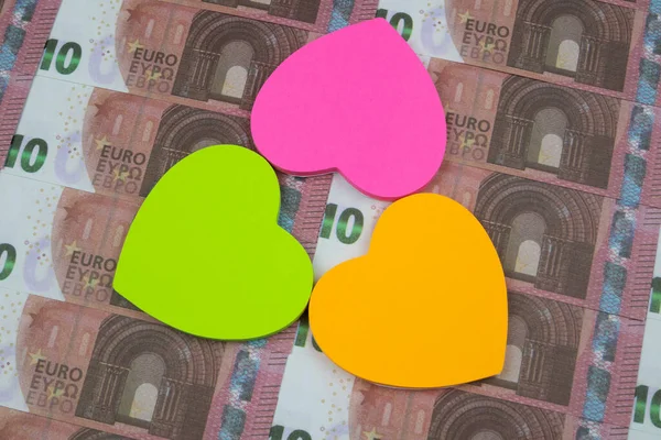 Three colored stickers in the form of hearts lie on 10 Euro banknotes