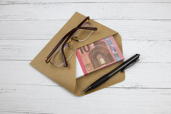 Glasses, black pen and an envelope with a bundle of 10 Euro bills lie on a table