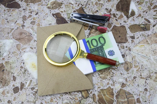 Une loupe repose sur une enveloppe avec un paquet de 100 euros sur la table — Photo