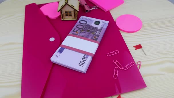 A pack of 500 euros of bills is lying with pink stationery rotating on the table — ストック動画