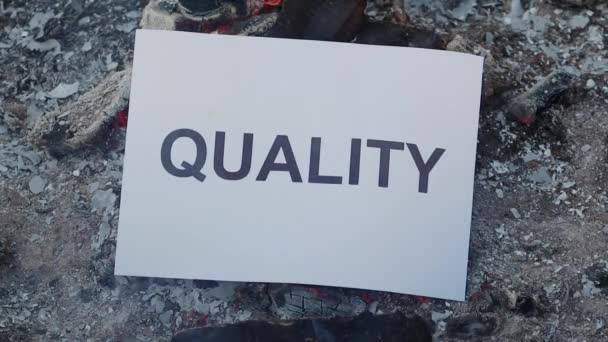 Word Quality sur une feuille de papier blanc brûle dans un feu contre. Mouvement lent — Video