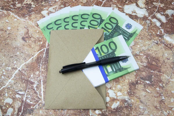 Caneta e envelope preto com notas de 100 euros encontra-se numa mesa de pedra — Fotografia de Stock