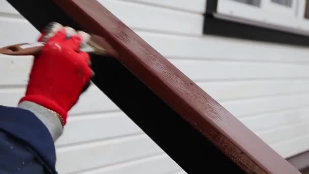 Mulher trabalhadora em luvas vermelhas pinta um corrimão de madeira perto de uma casa branca marrom — Vídeo de Stock