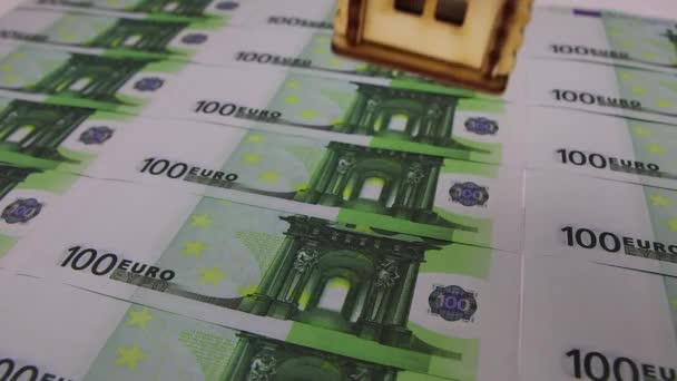 Mão em luva branca coloca uma pequena casa de madeira em notas de 100 euros — Vídeo de Stock